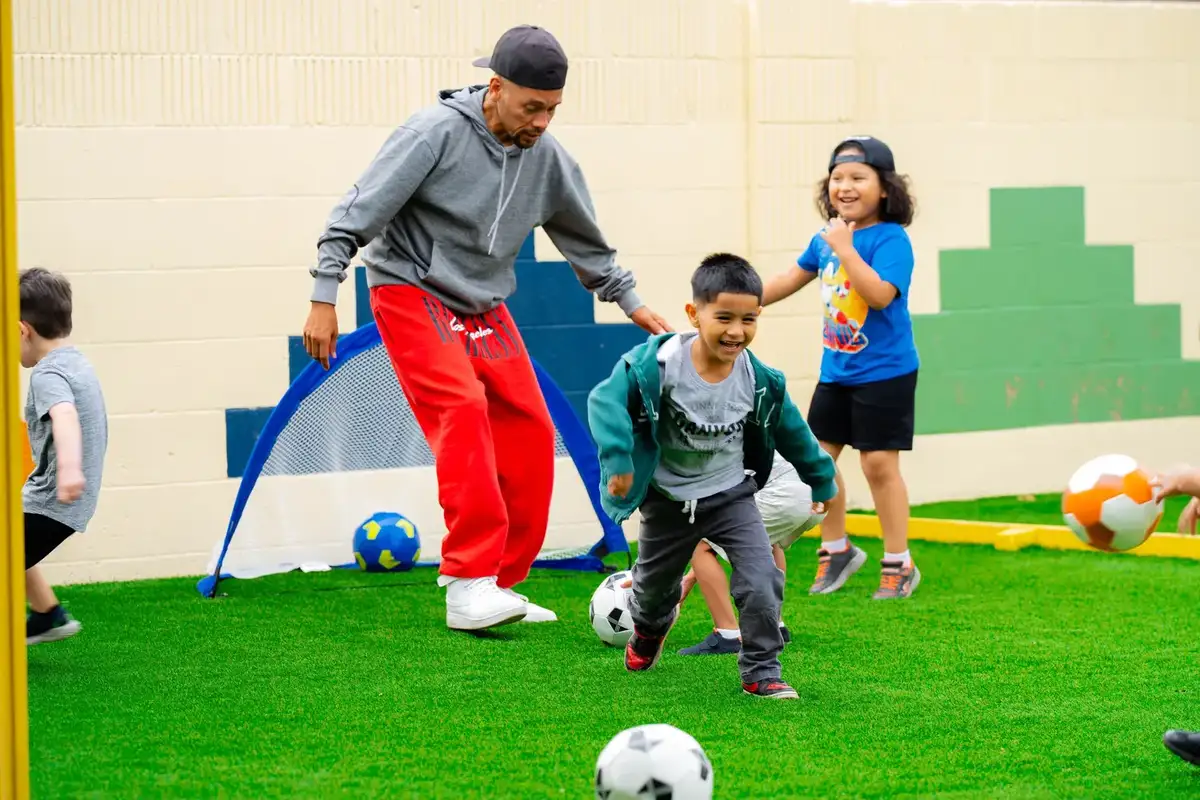 Children playing soccer outdoors with an instructor during enrichment at Newport Ave Preschool