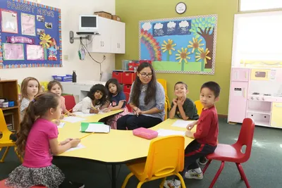Qualified and caring preschool teacher doing an activity with children, everyone smiling in a supportive learning environment at Newport Ave Preschool