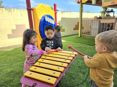 Children playing musical instruments outdoors during a music enrichment lesson at Newport Ave Preschool
