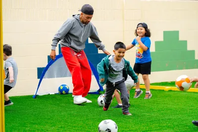 Children playing soccer outdoors with an instructor during enrichment at Newport Ave Preschool